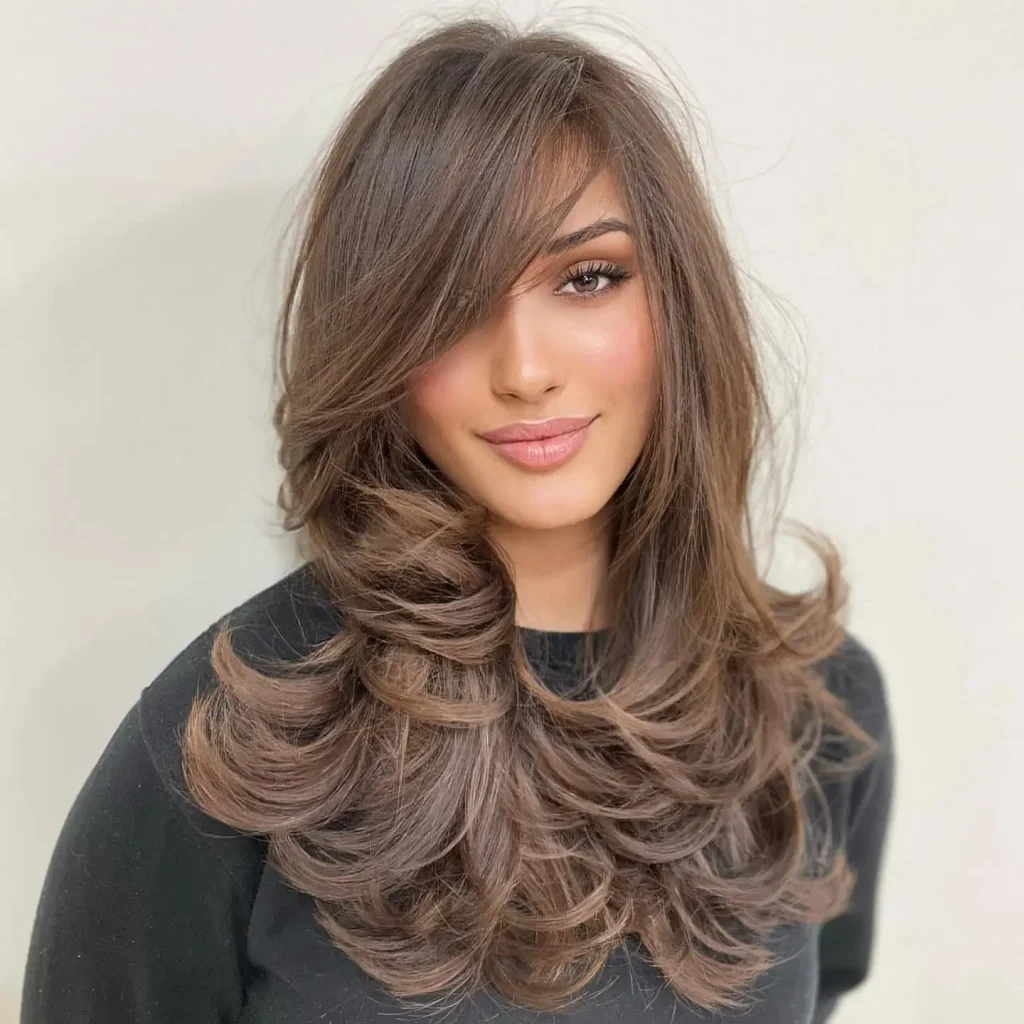 Medium-length honey-brown layered hair with outward-flipped ends, softly lifted roots, smooth feathered layers, a glossy blowout, and a polished retro-inspired beauty photograph in warm studio lighting.