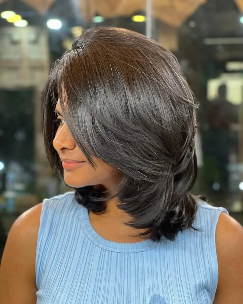 Thick, dark-brown hair cut to the shoulders with blended layers that reduce bulk, smooth movement through the mid-lengths, softly curved ends, and a glossy three-quarter rear-view salon photograph.