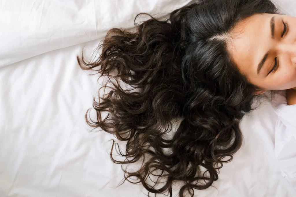 Long glossy overnight heatless curls created with a satin curling rod, soft bouncy spirals, natural brunette hair, morning window light, front three-quarter salon editorial portrait.