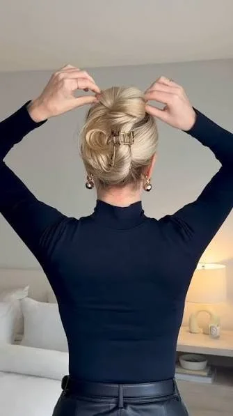 Medium-length dark brunette hair styled in a French twist secured with a large neutral claw clip, soft loose ends tucked neatly, modern everyday look, side-back view, natural indoor light.
