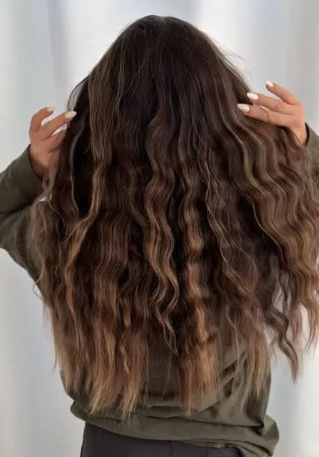 Long soft waves revealed after overnight braiding, natural brunette-to-caramel hair, loose uniform bends, healthy shine, morning window light, rear three-quarter view.