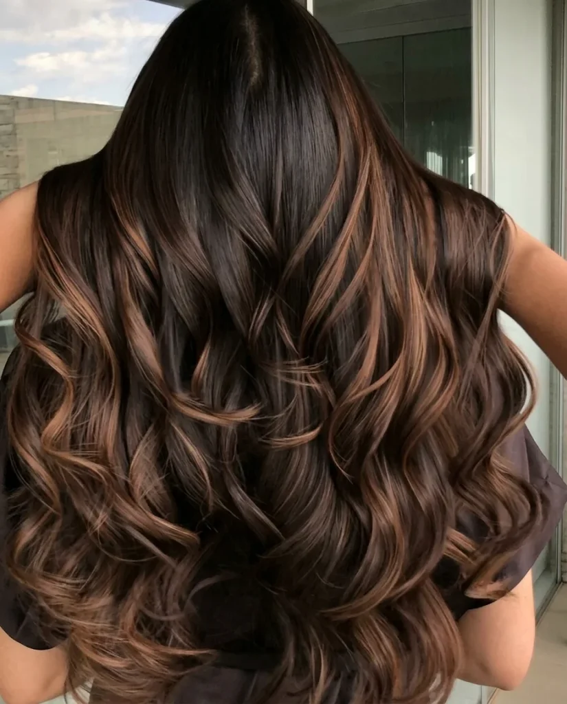 back view of long dark-chocolate hair with caramel ribbons through deep, voluminous curls, bright window light