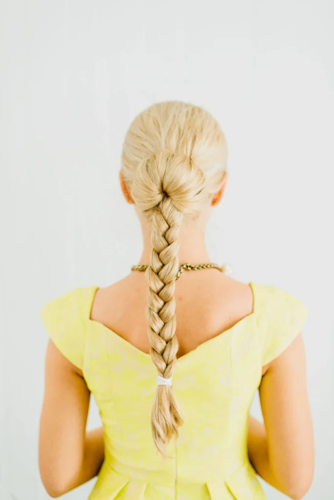 Elegant French braid starting at the crown and continuing down long brown hair, neat woven sections, natural texture, rear head view, soft salon lighting.