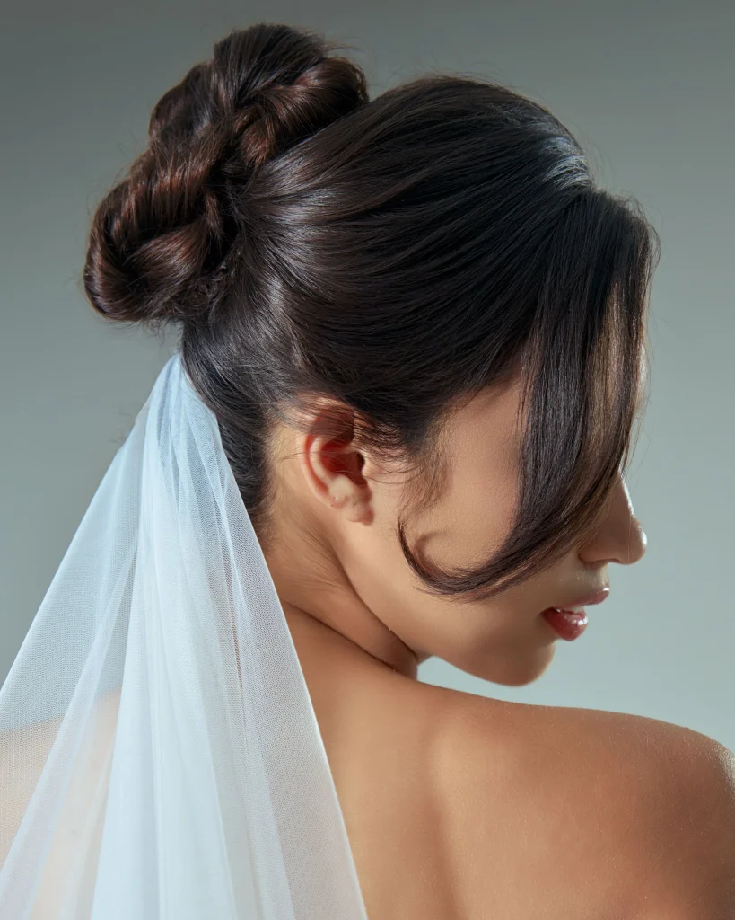 Sleek low bun at the nape of the neck, smooth center-parted dark brown hair, elegant minimalist finish, visible natural shine, neutral studio background, rear three-quarter portrait.