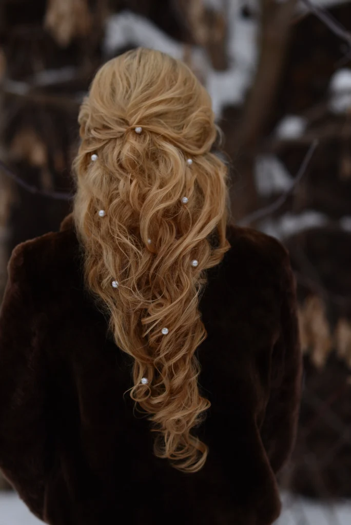 Half-up half-down hairstyle on long chestnut hair, top section secured at the back with a small clip, natural loose waves, soft face-framing pieces, bright window light, rear three-quarter portrait.