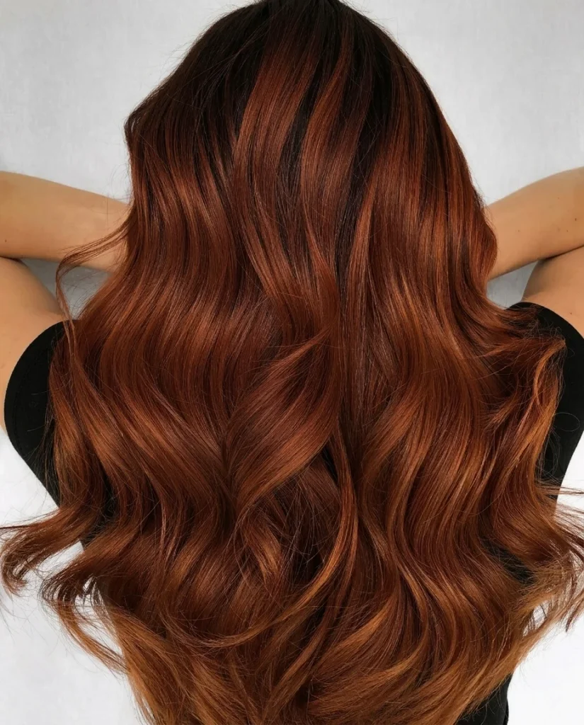 back view of long cinnamon-copper waves with a dark shadow root, studio backdrop, hands lifted