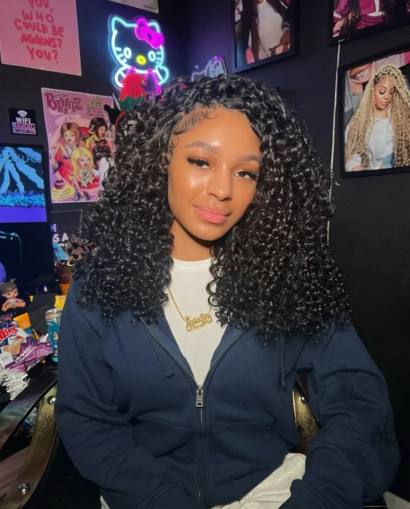 smiling woman with a shoulder-length bouncy black curly bob, defined spiral curls and a neat side part, navy zip hoodie, colorful pink neon-lit room
