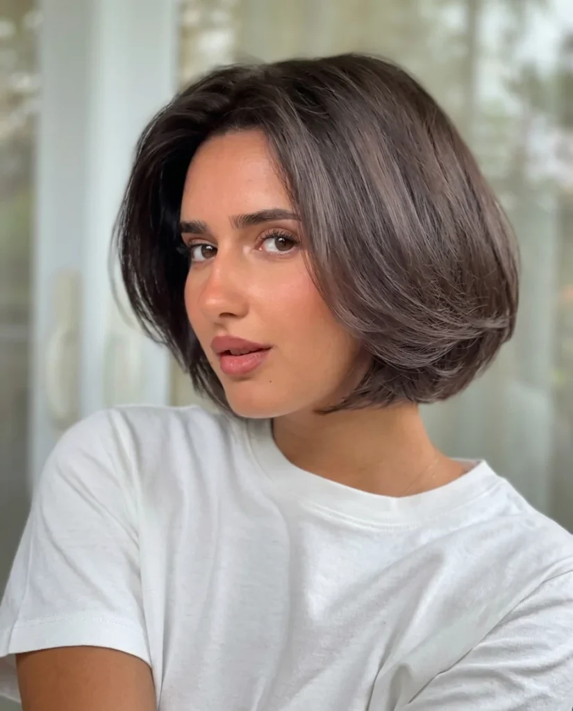 woman with a rounded, layered mushroom-brown bob with a deep side part and glossy finish, white tee, soft window light
